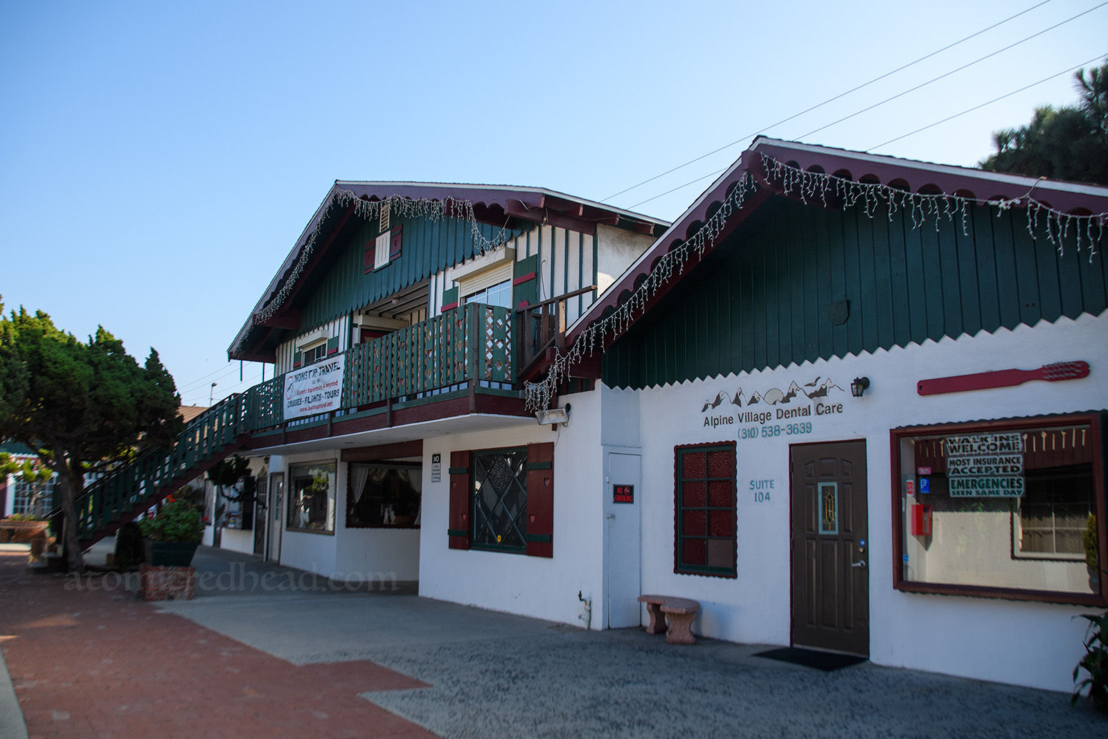 Angled view of a two story portion of the village. The upper half painted a forest green, the lower half painted white with scalloped edged doors and windows. A large toothbrush hangs above a window advertising the dentist inside.