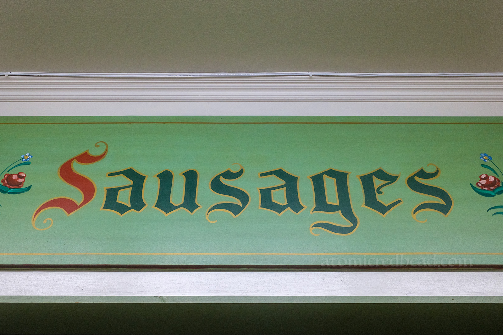 A large green sign, hand painted to read "Sausages"