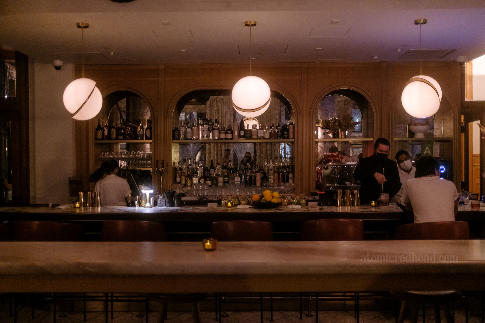 Overall view of the bar, which features an mirrored, arched bar back, and three globe light fixtures that hang over.