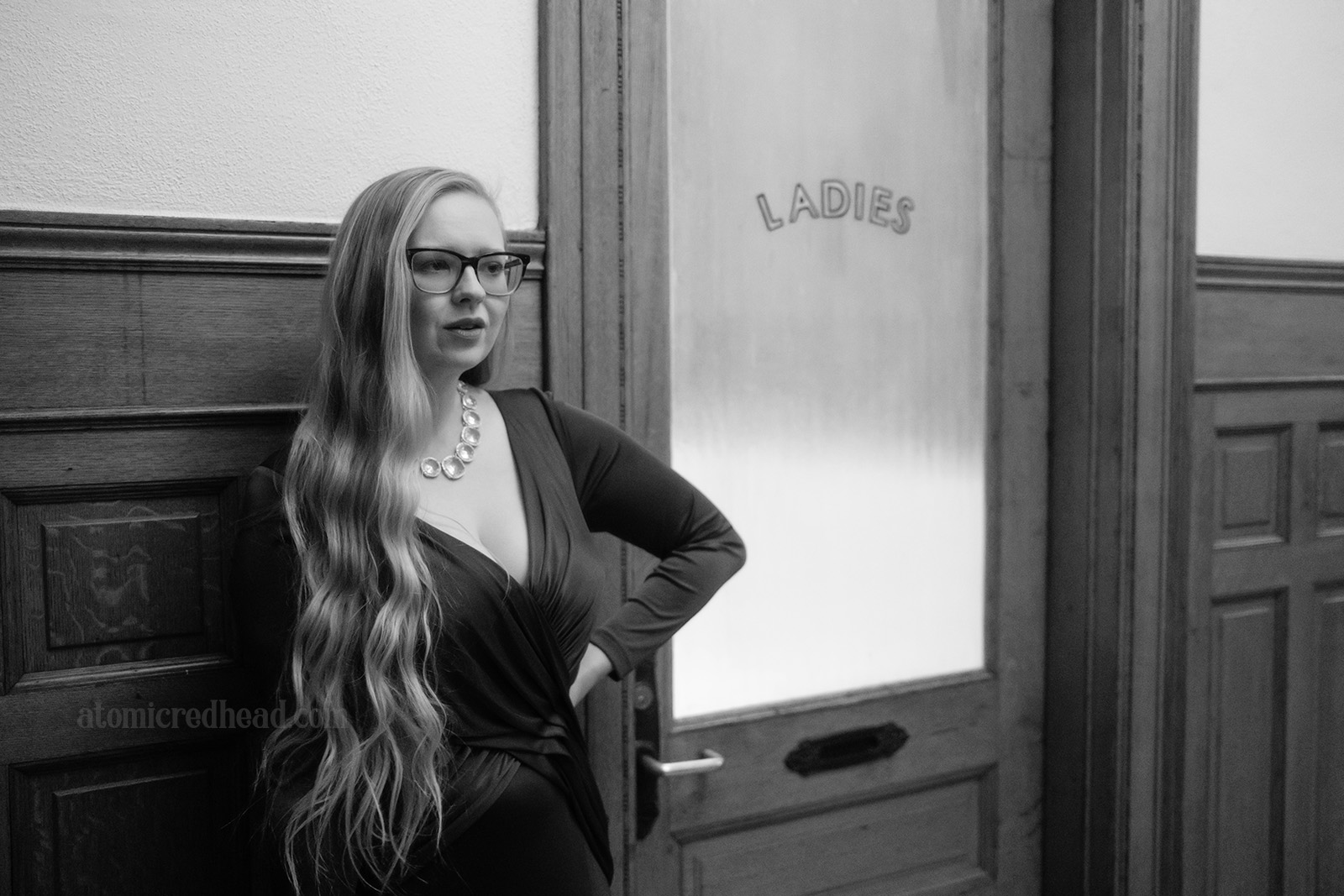 Black and white photo of myself standing in front of a frosted glass door reading "Ladies" painted on it.