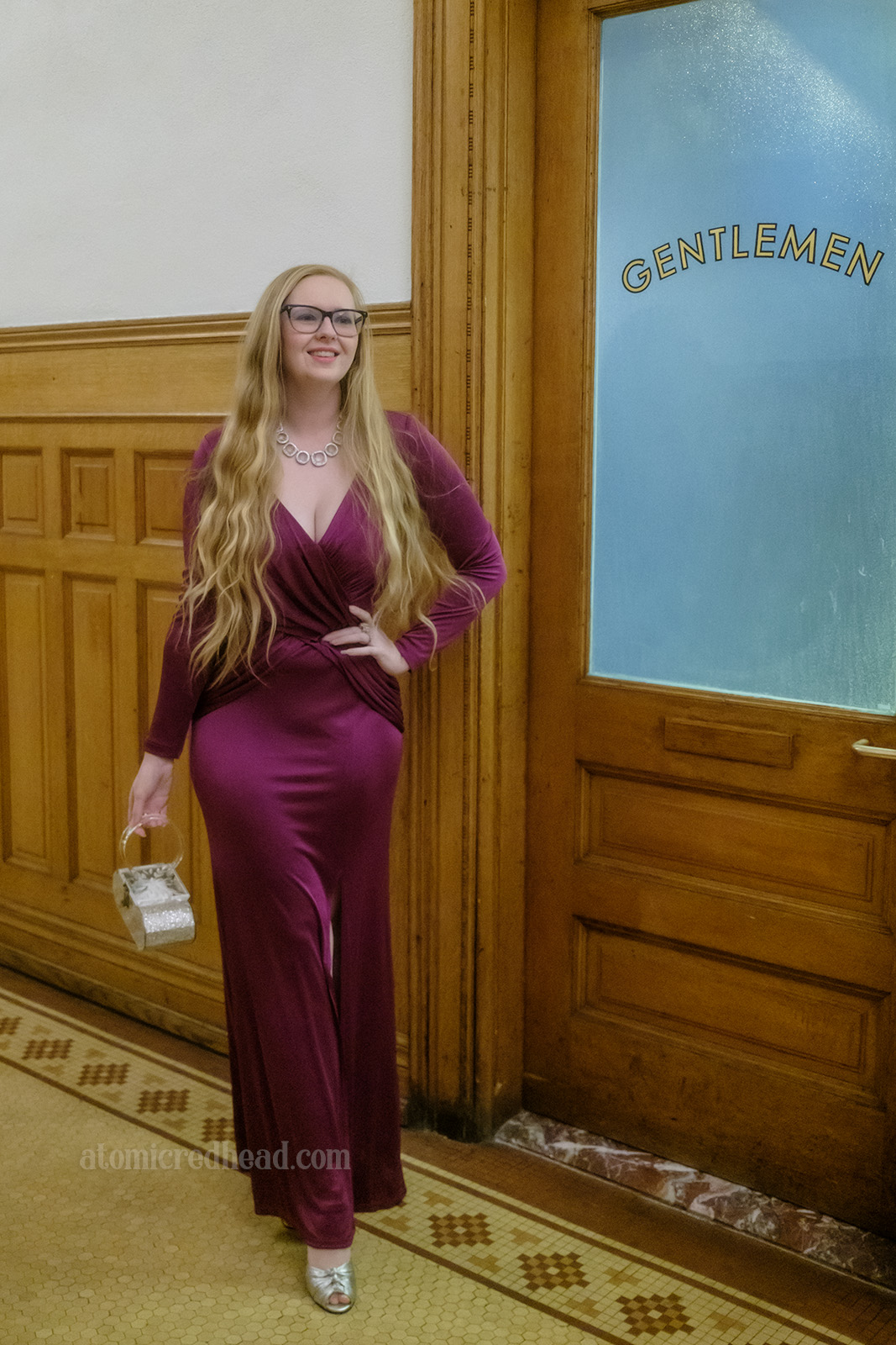 Myself, wearing a floor length purple gown, standing in front of a frosted glass door reading "Gentlemen" painted on it.