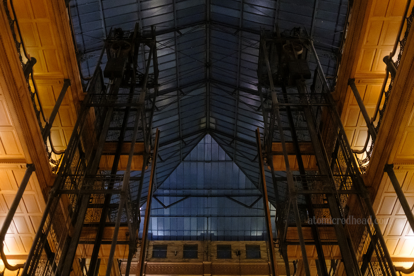 Looking up toward the massive atrium glass roof, the open cage elevator shafts flank either side.