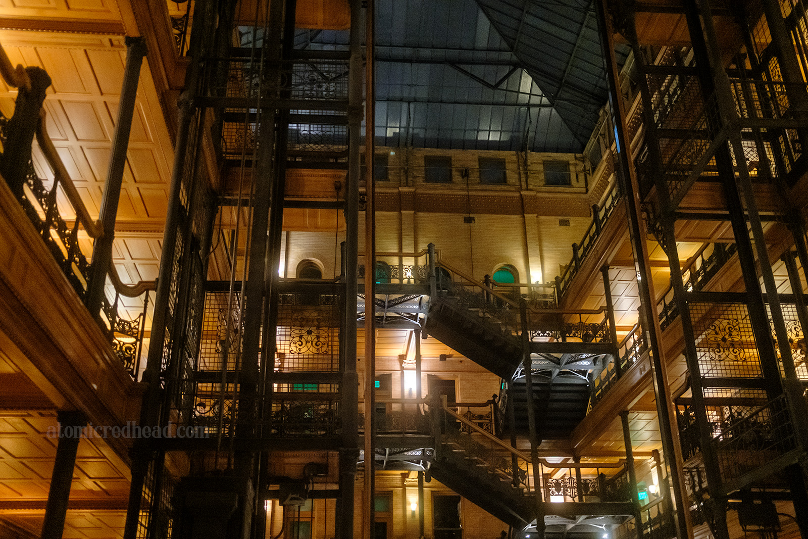 Interior of the Bradbury, with the open elevator shaft on the right, and the zig-zag staircase on the right. Black wrought iron makes up railings and balconies in front of light wood paneled walls.