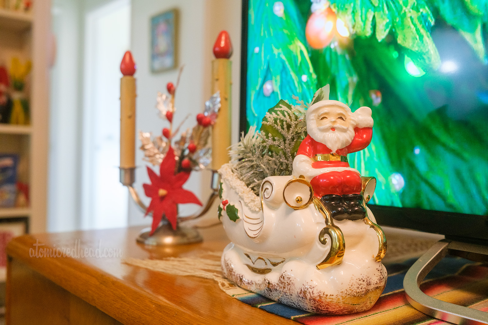 A small ceramic planner of Santa sitting atop his sleigh, it is filled with greenery.