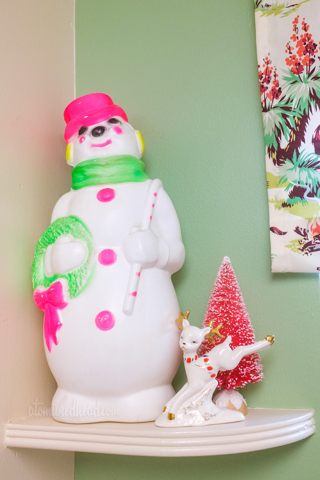 Close-up of one kitchen shelf, which features a small blow-mold snowman, and very small ceramic reindeer.