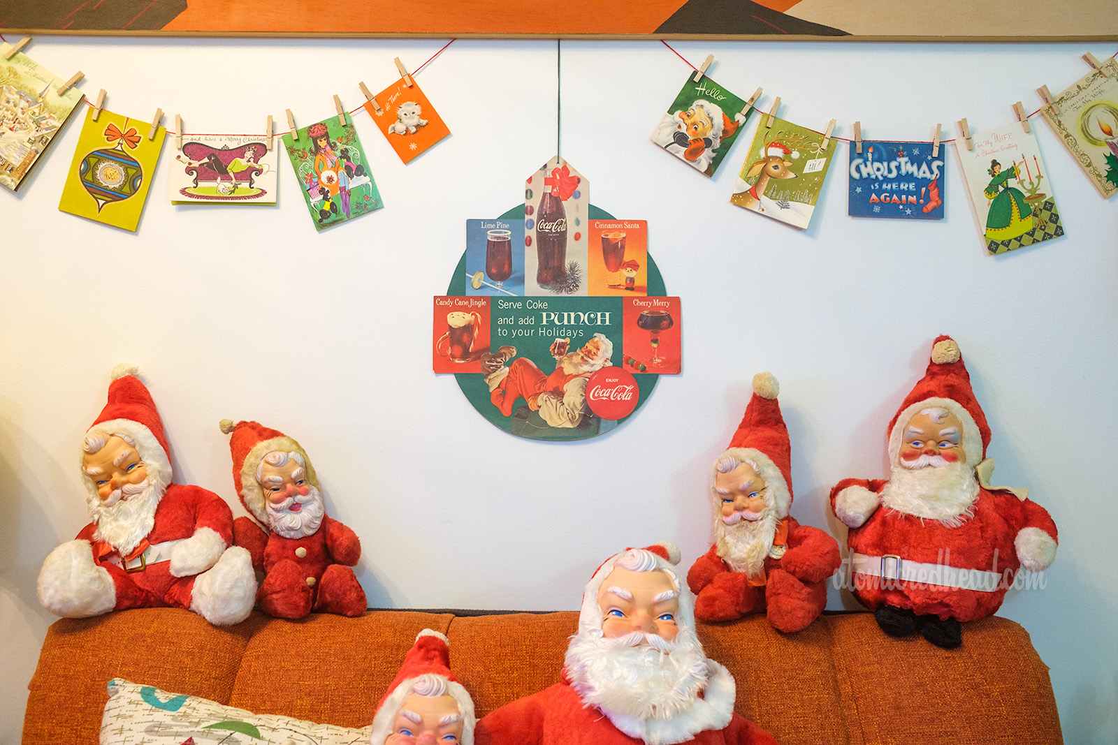Close-up view of the various Christmas cards above the couch. In the middle is a Coca-Cola advertisement with Santa sitting drinking a Coke.