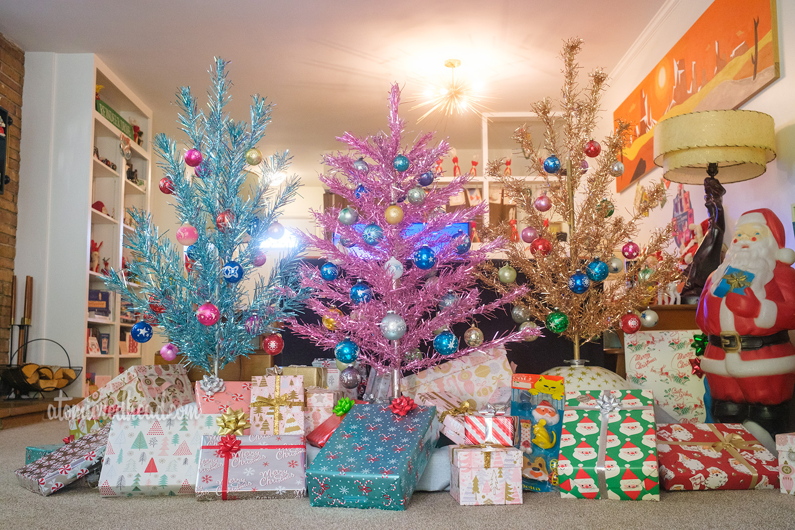 Three aluminum trees, each roughly four feet, stand together, one blue, one pink, and the third one gold. Under them are a variety of wrapped gifts.