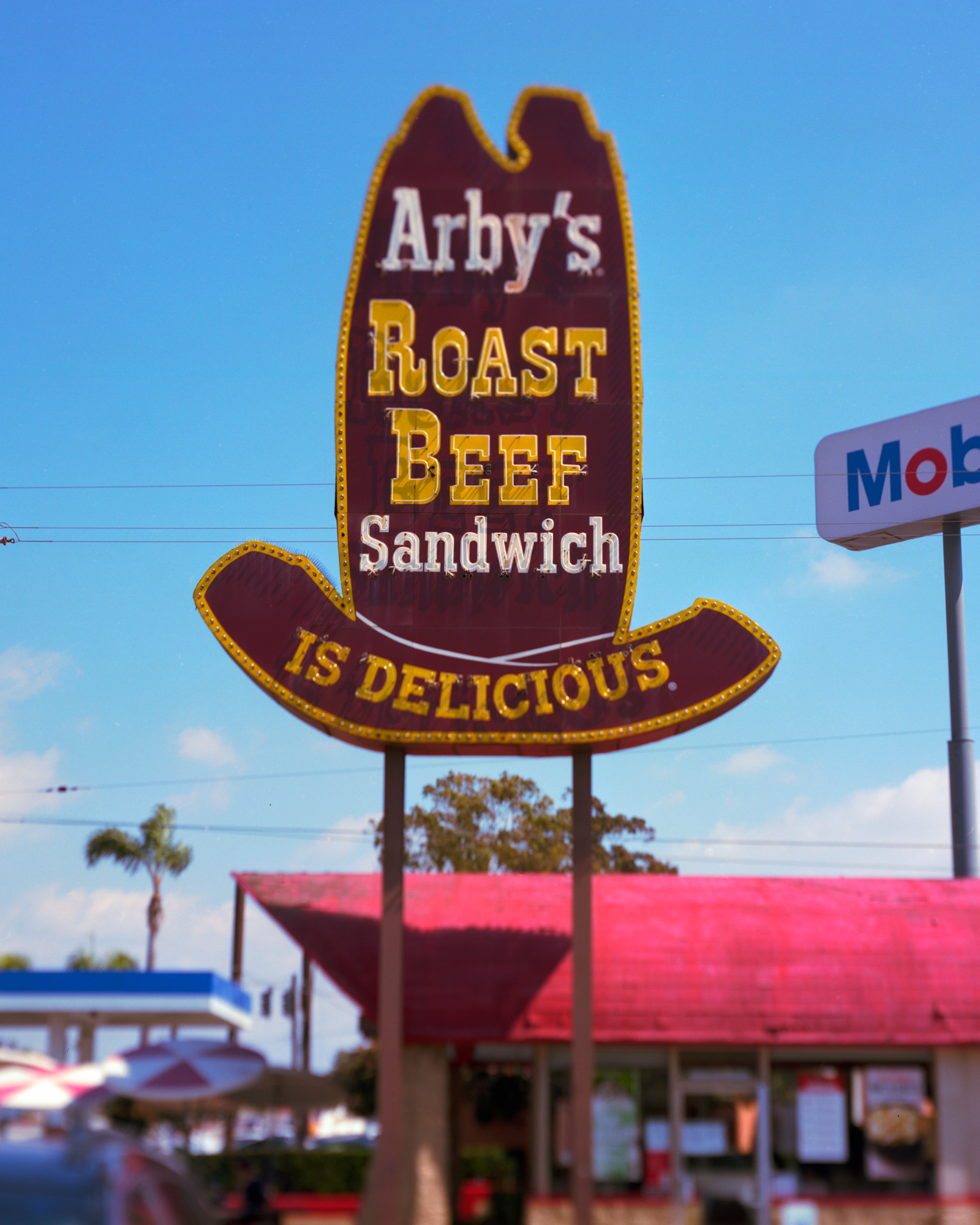 Photo of an Arbys sign in the shape of a tall cowboy hat that reads "Arby's Roast Beef Sandwhich Is Delicous"