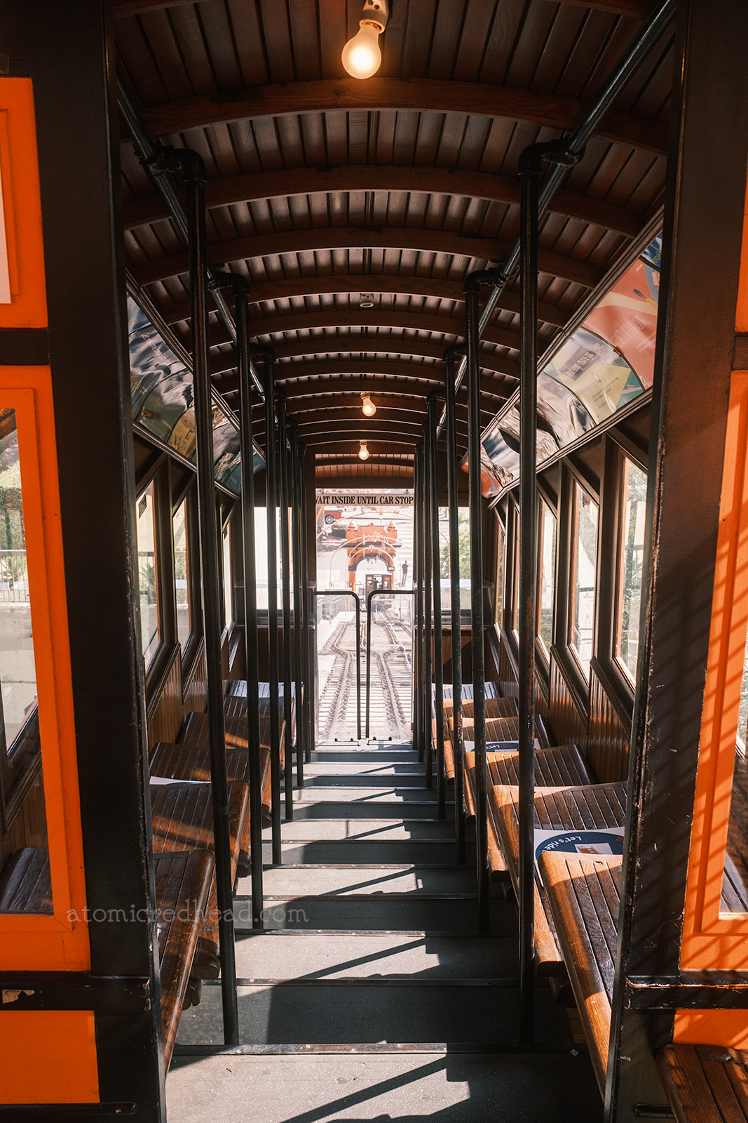 View of the inside of one of the cars. Dark wood paneled walls and seats, which are done in a stair step format. 