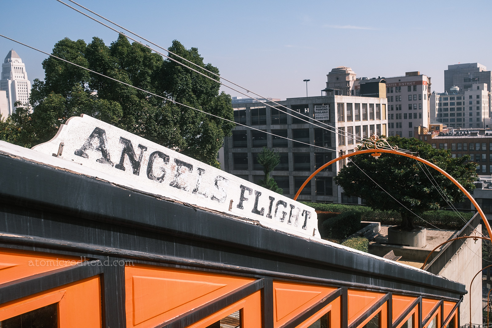 Close-up of the white sign atop one of the cars, which is white and reads "Angels Flight" in faded black letters. LA City Hall is visible in the distance.