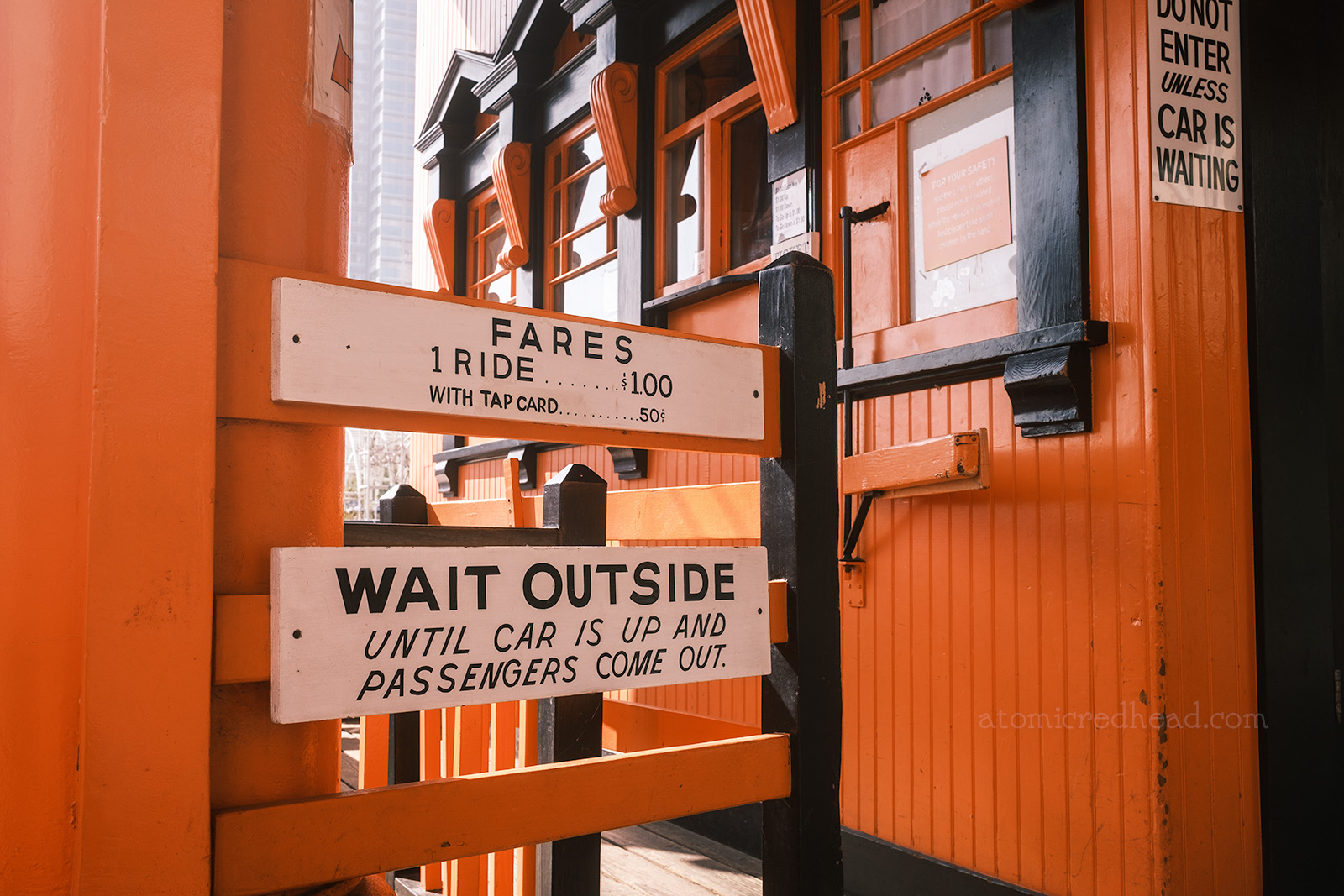 Gate at the Grand Avenue station with various signs reading "Fares 1 Ride $1.00 With Tap Card .50" "Wait Outside Until Car is Up and Passengers Come Out." 
