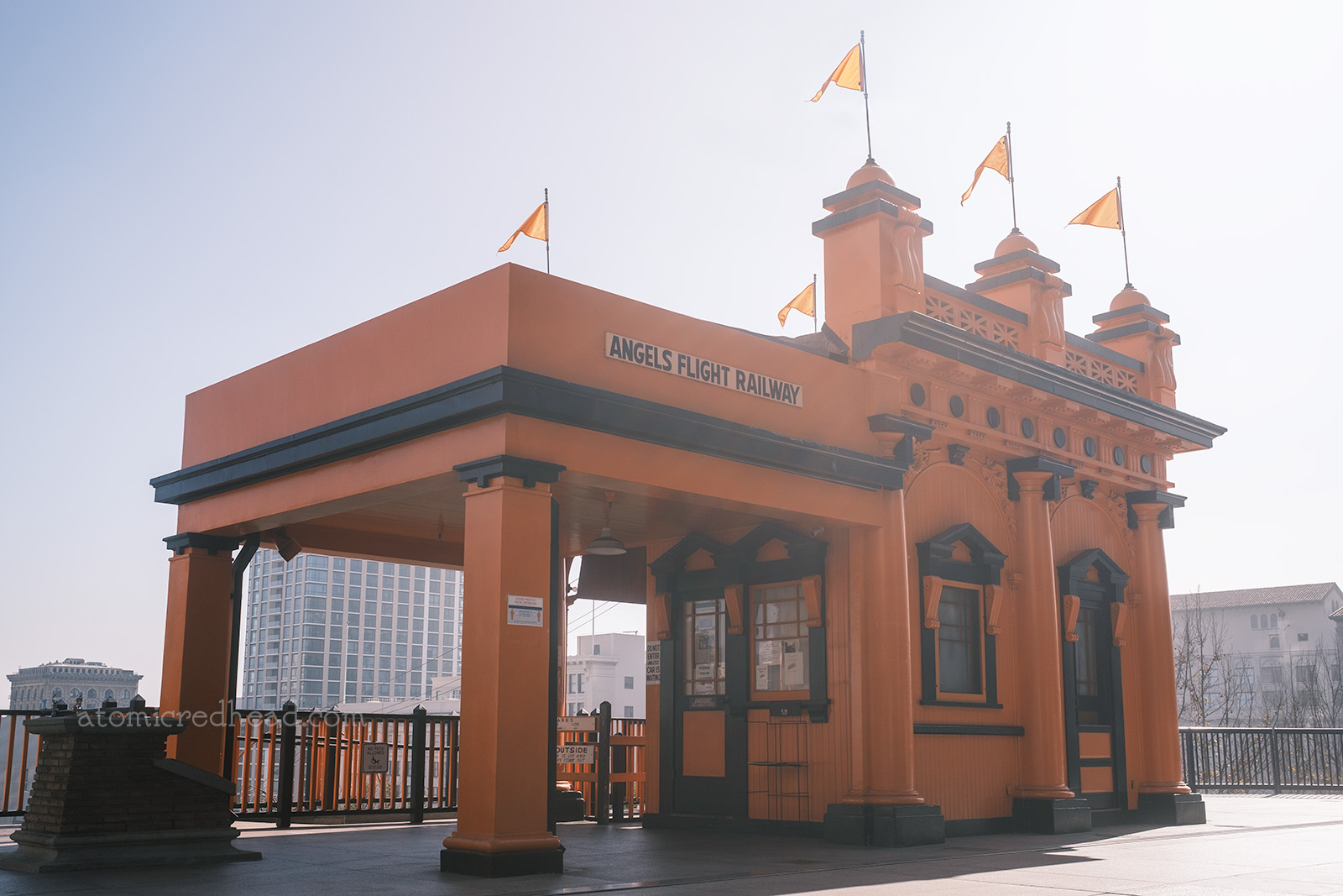 The Grand Avenue station building, which holds the operator, painted orange with black trim. Small flags are at the top. A sign on the left reads "Angels Flight"