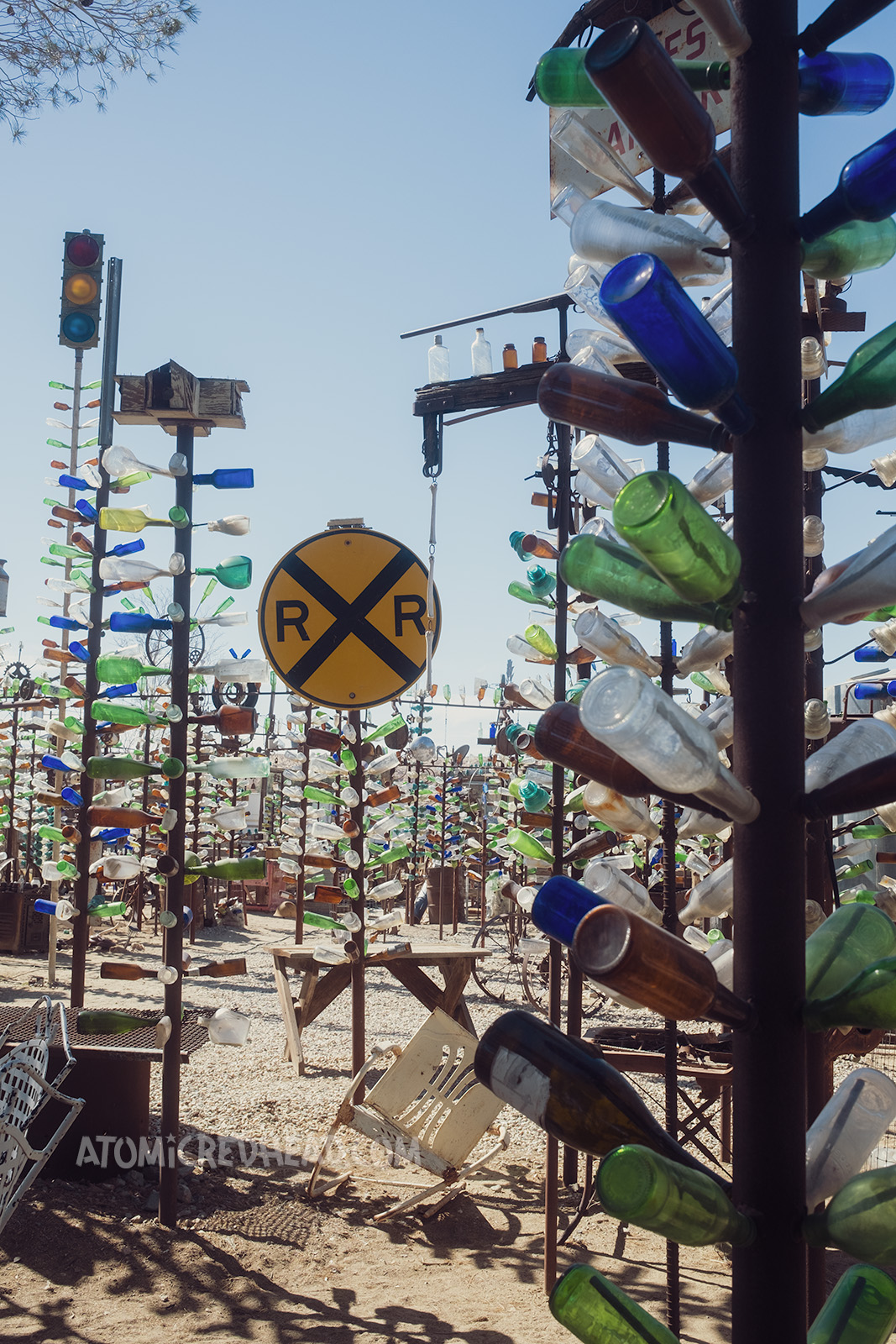 Wide, overall shot of Bottle Tree Ranch. The "bottle trees" are tall metal posts with smaller rods jutting out from the side, with glass bottles slid onto them. Some of the trees are topped with various items, such as wheels, lanterns, and signs.