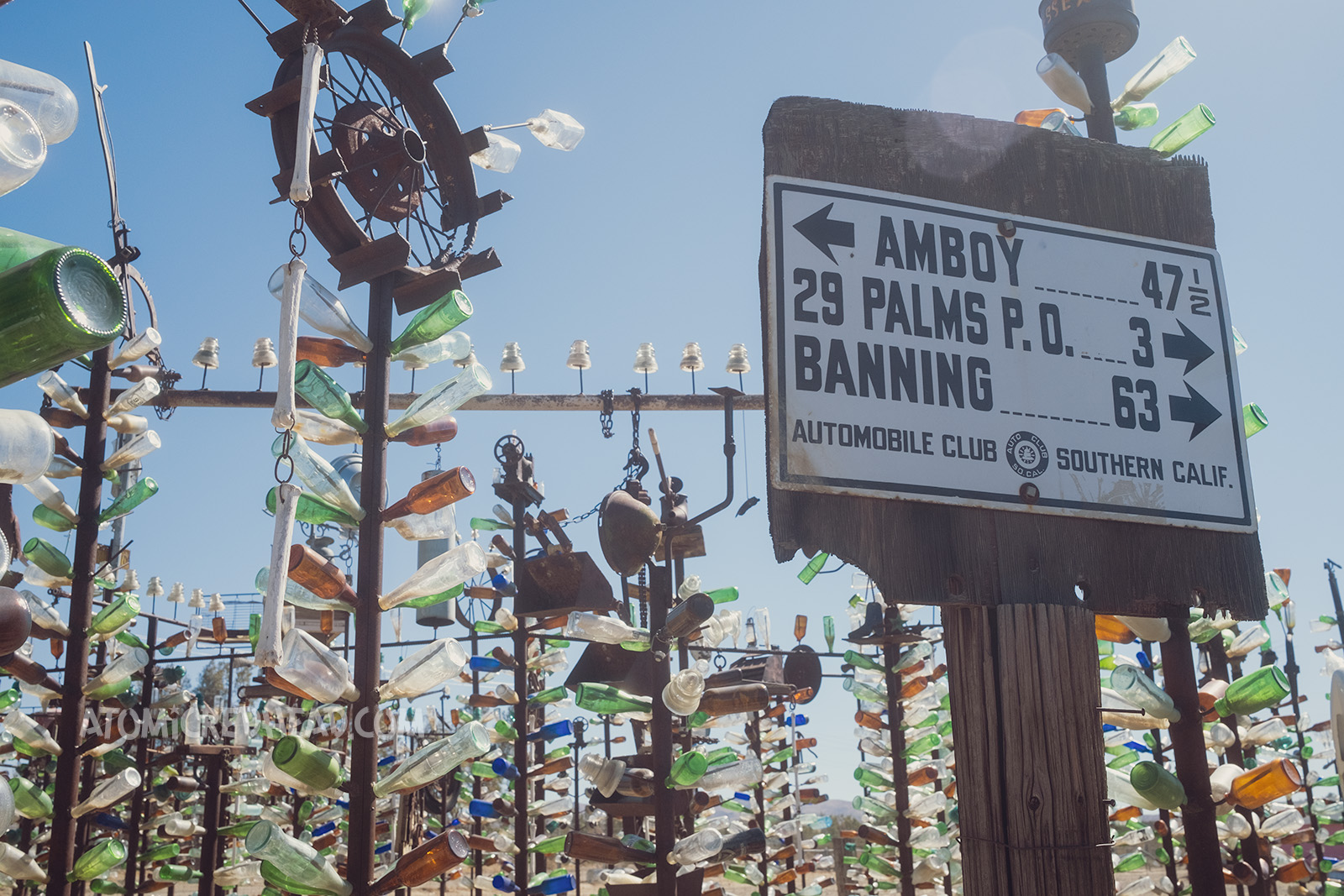 Various bottle trees, and a vintage sign reading the distances to other desert towns, including Amboy, 29 Palms, and Banning.