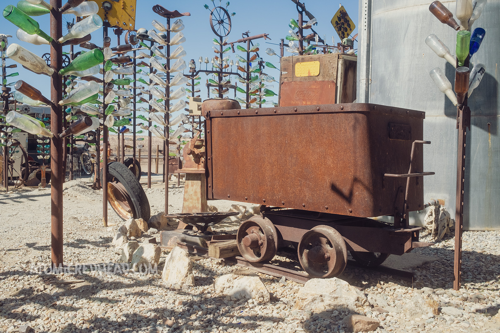 An old, rusted mine car sits amid the various bottle trees.