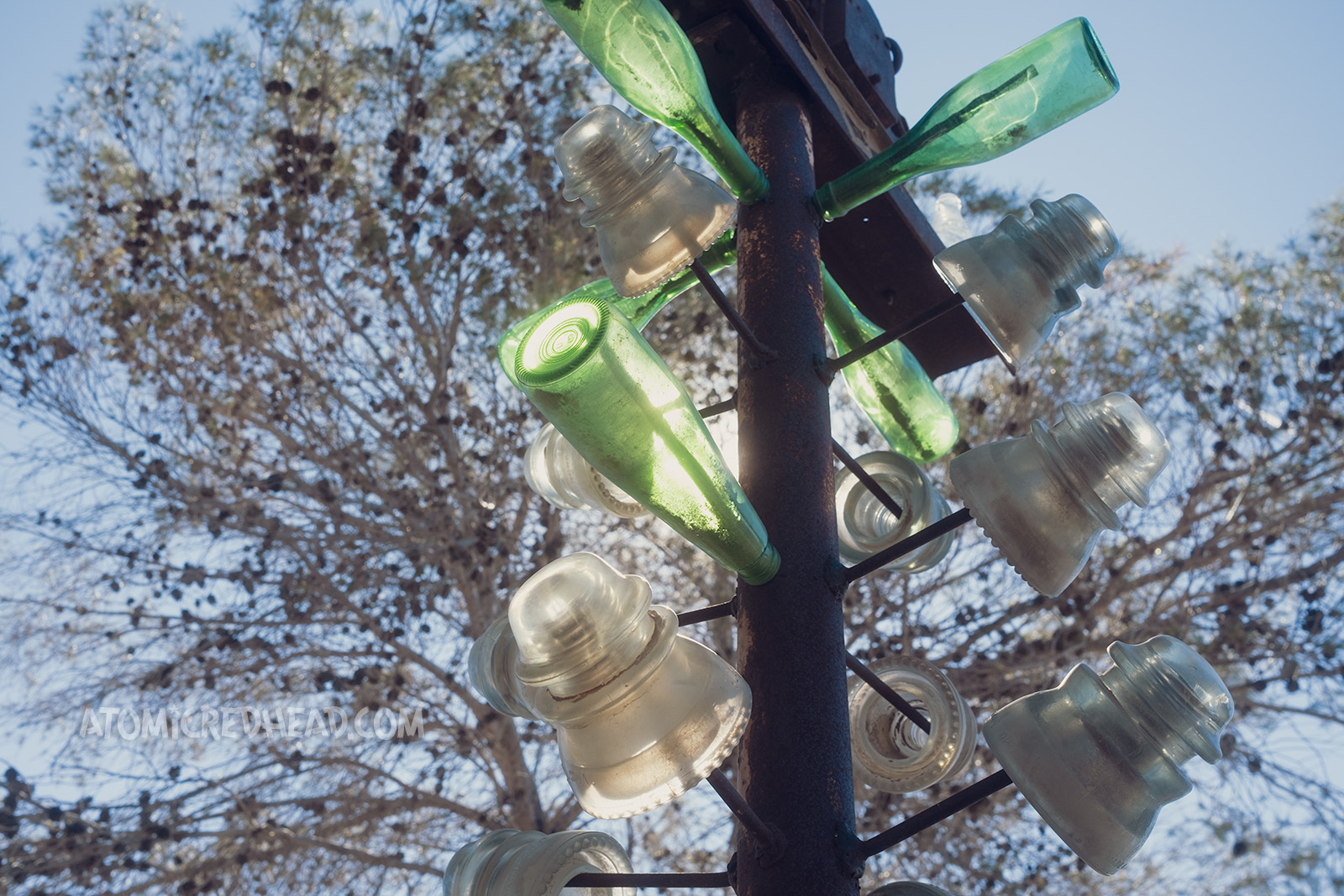 Close-up of some bottles and vintage insulators hang on one of the bottle trees.