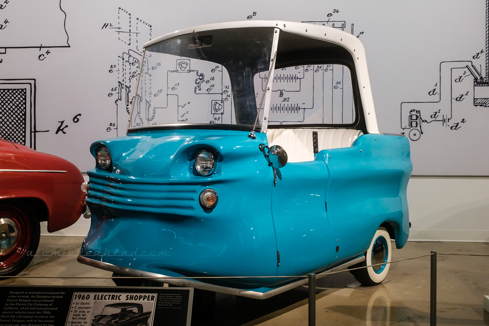 And early electric car known as "The Shopper" from 1960. A small, almost glorified golf cart, painted blue with a white top, small little fins peek in the back.