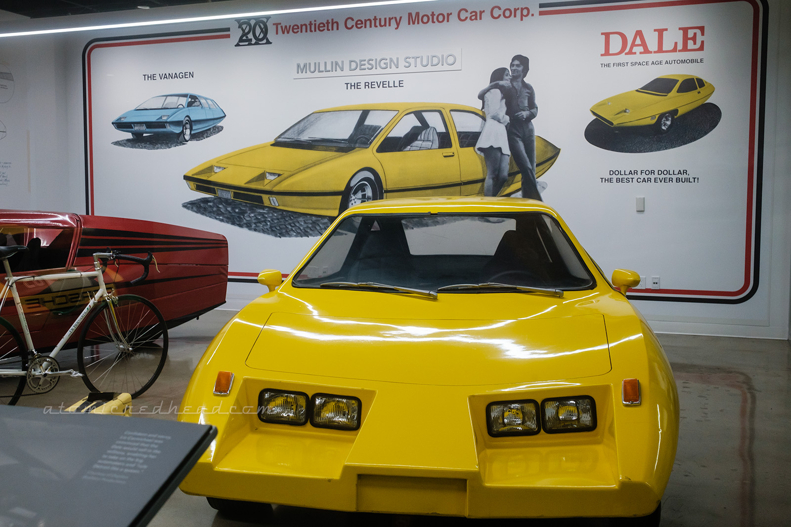 The yellow Dale prototype, from 1974, which features four headlights, and three wheels. Behind it the wall features a blown up illustration of the concept.