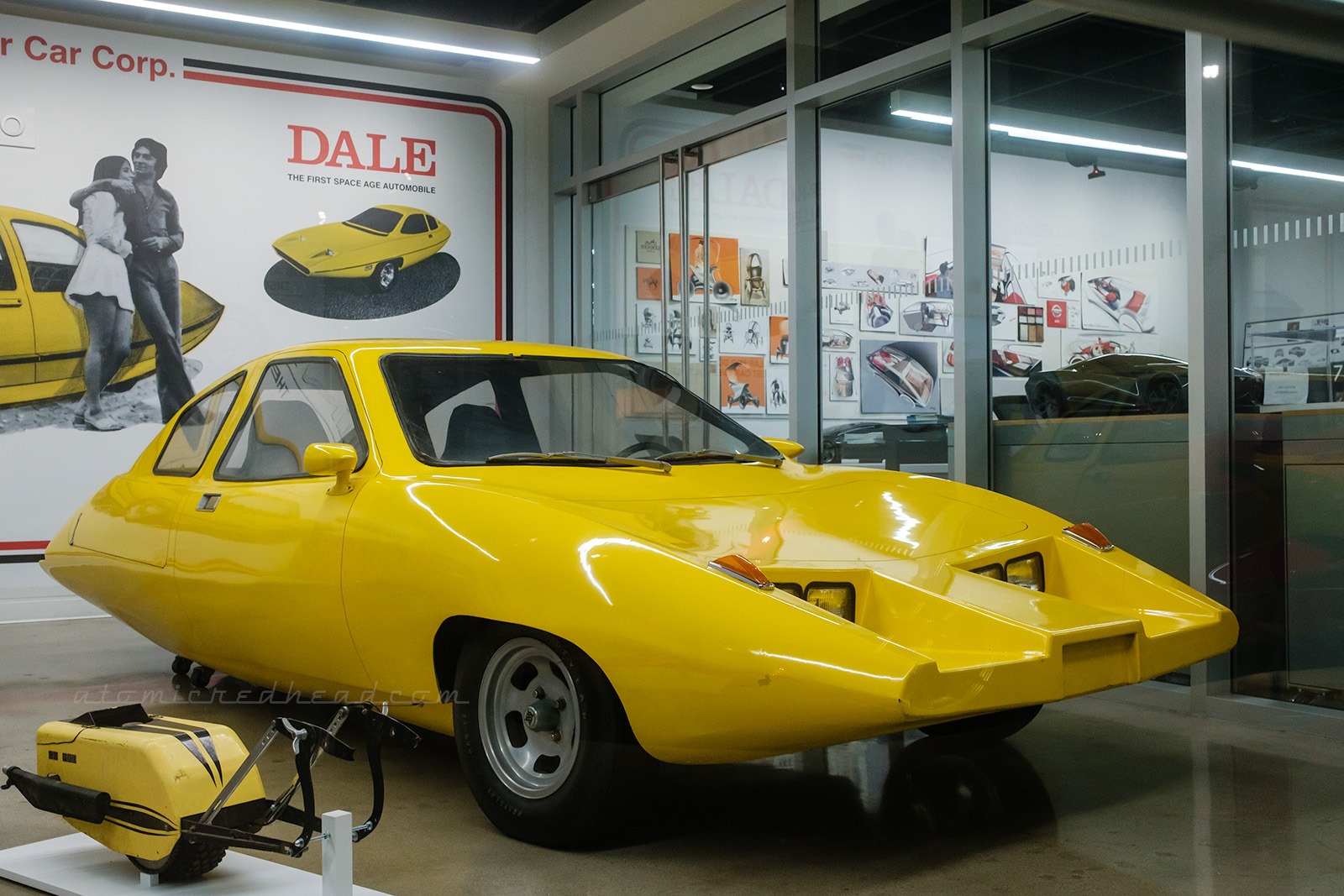 The yellow Dale prototype, from 1974, which features four headlights, and three wheels. Behind it the wall features a blown up illustration of the concept.