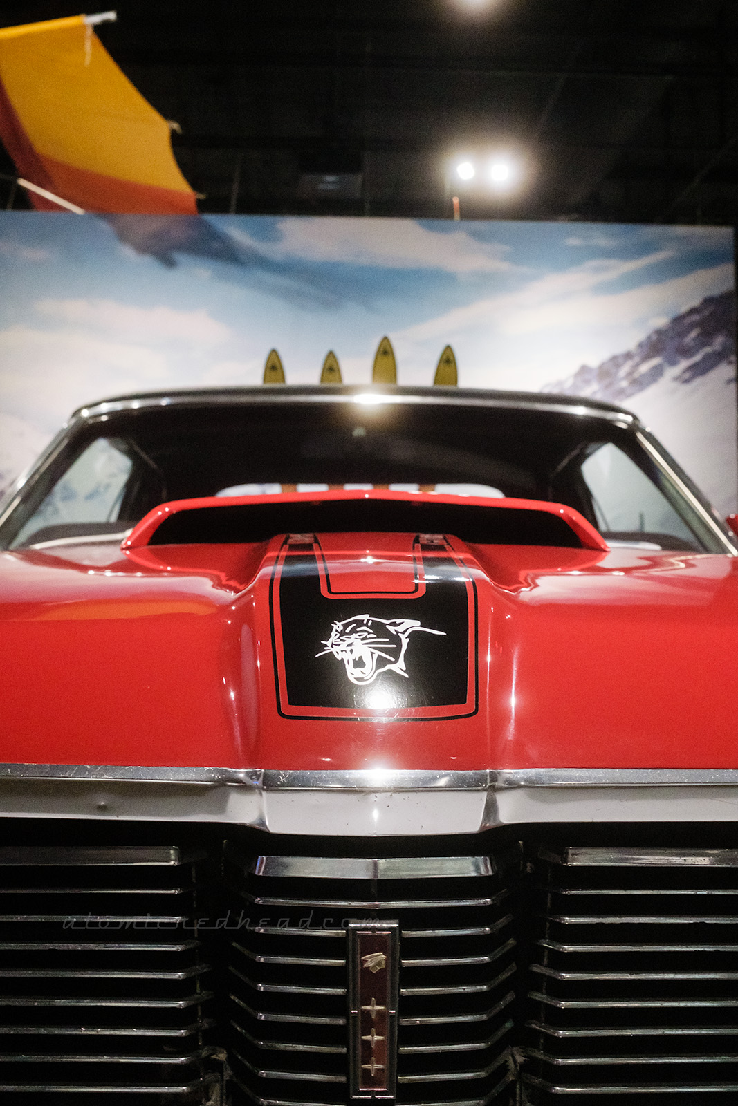 The 1969 Mercury Cougar XR-7 as seen in On Her Majesty's Secret Service and driving by Diana Rigg's character. The red car features black details on the hood, including the silver head of a cougar in the center.