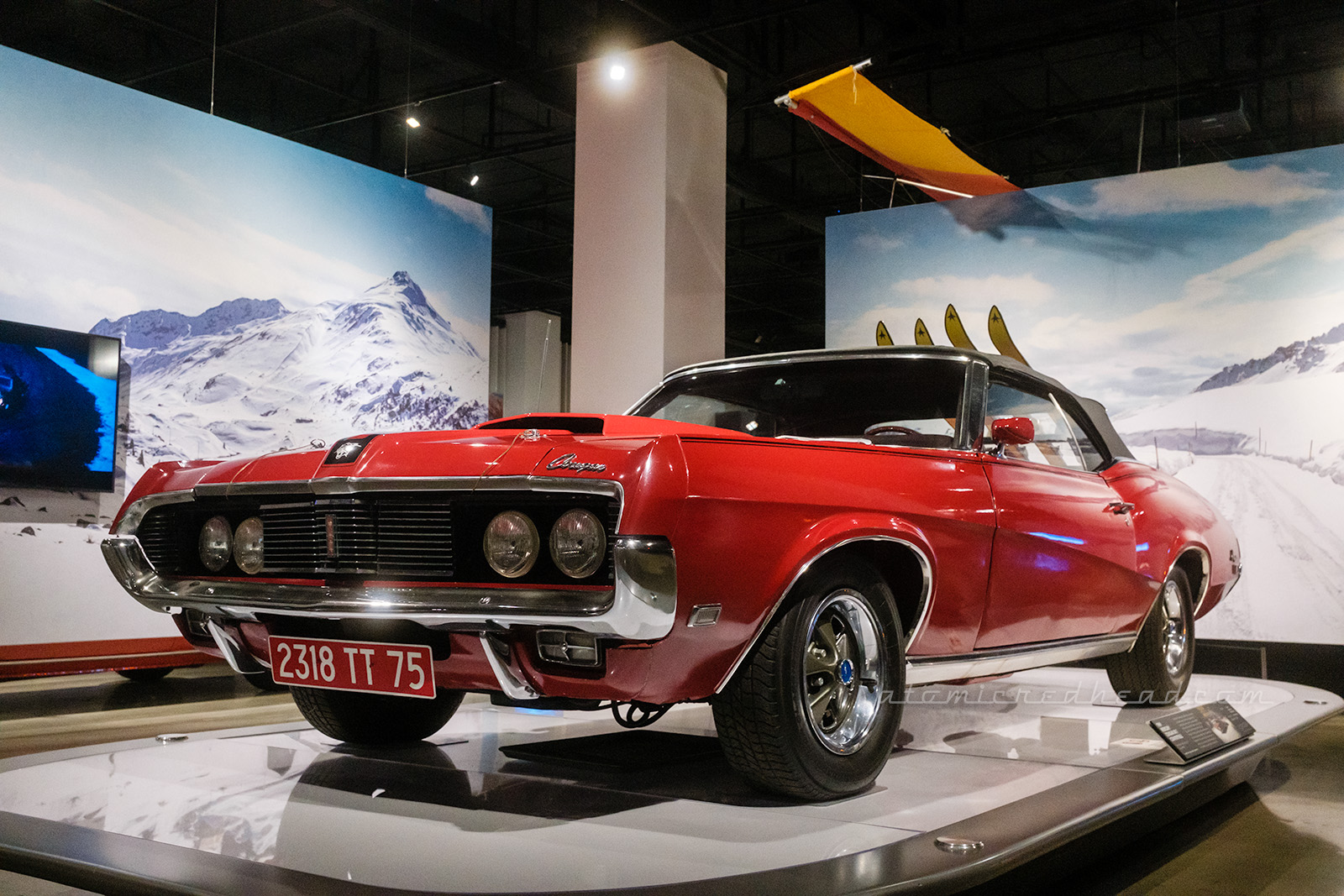 The 1969 Mercury Cougar XR-7 as seen in On Her Majesty's Secret Service and driving by Diana Rigg's character. The red car features black details on the hood, including the silver head of a cougar in the center.