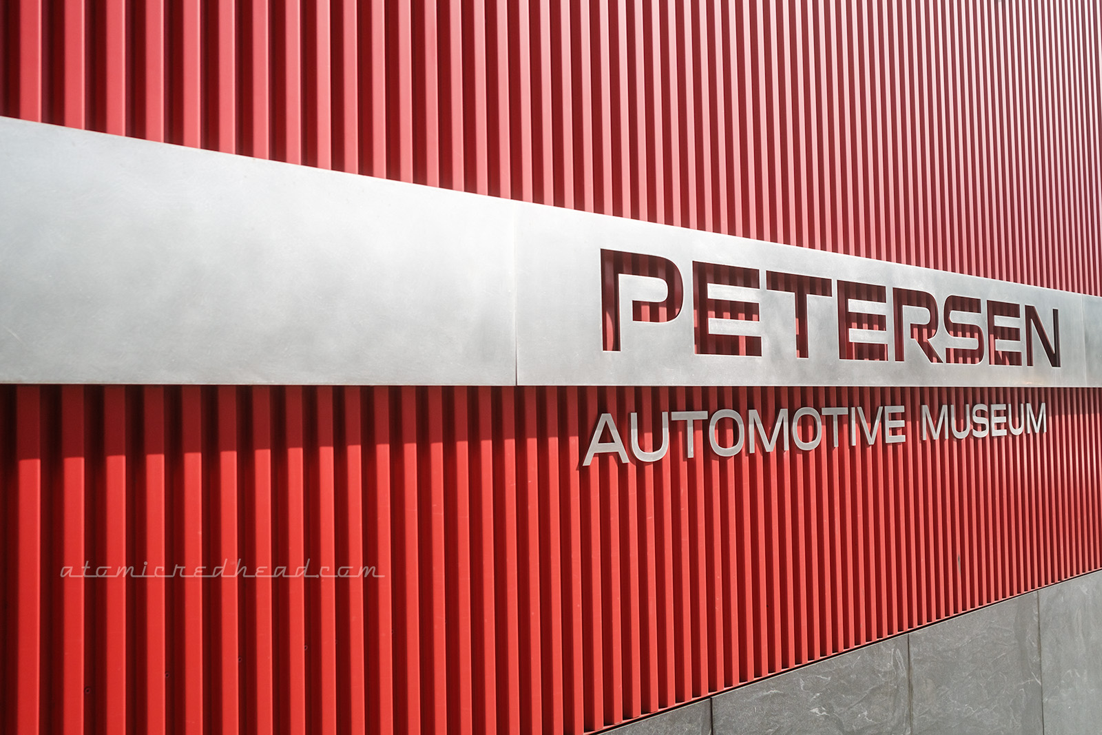 Side of the Petersen, which is made up of small red ribs, and a sleek piece of silver metal across, which reads "Petersen" in cut out letters, and "Automotive Museum" below.