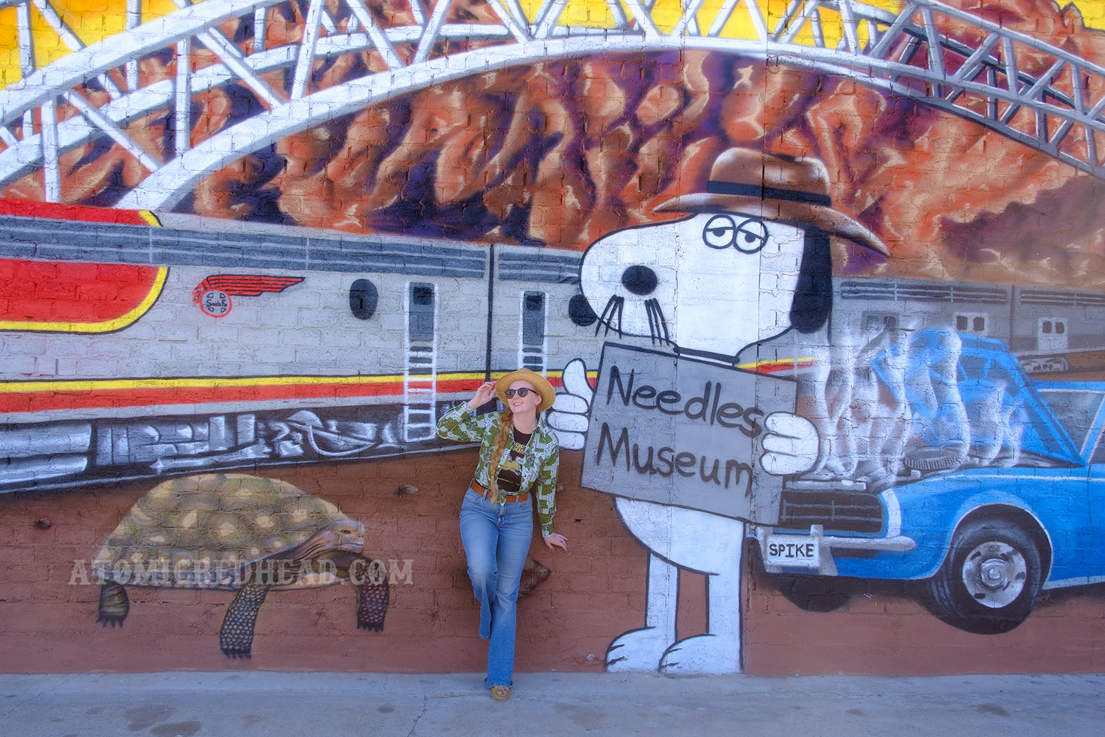 Myself standing in front of massive mural featuring a train, bridge, broken down car, and Spike, the cartoon beagle brother to Snoopy.