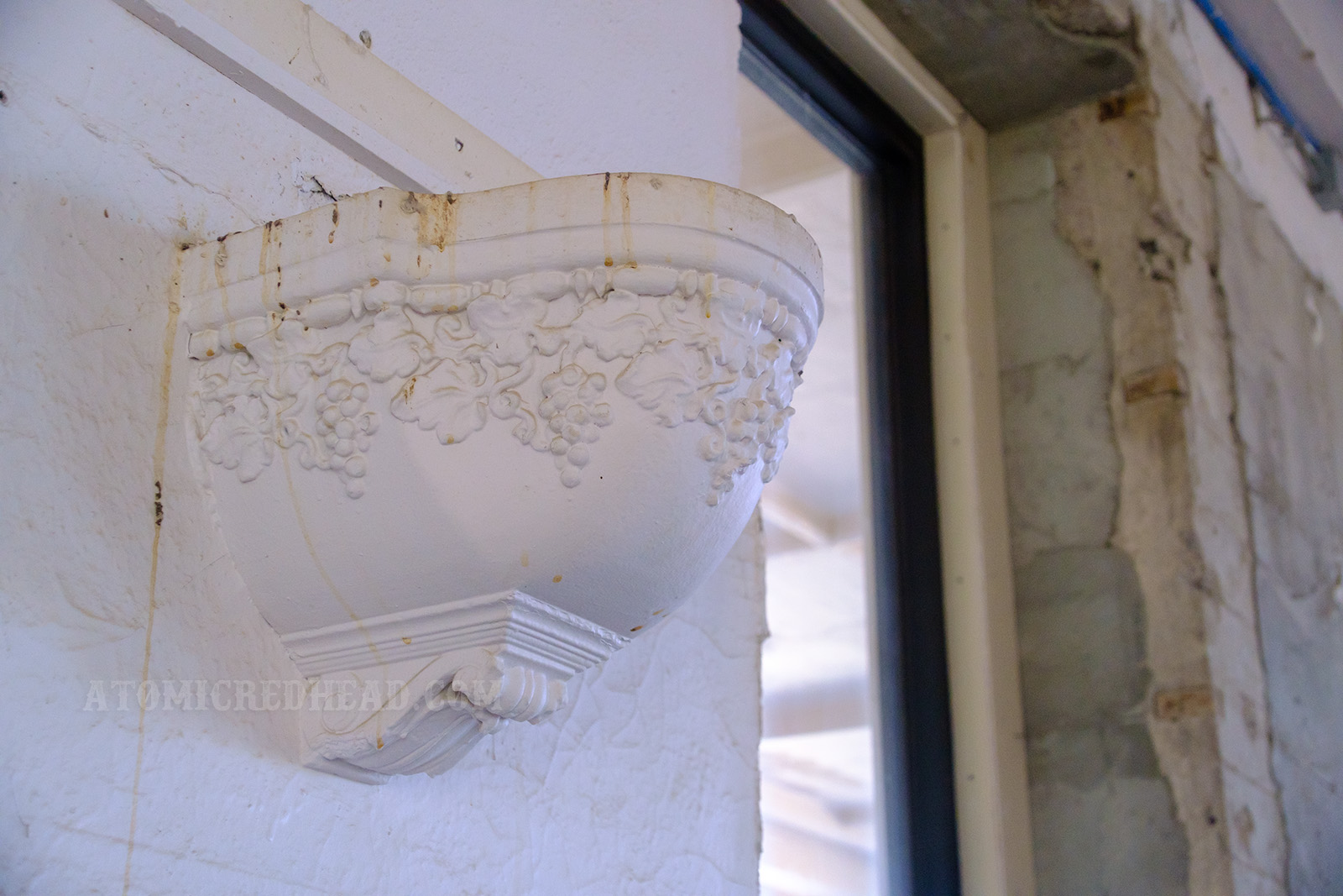 Close-up of one of the sconces, which may have once been light fixtures or planters. The detail showcases a design of grapes.