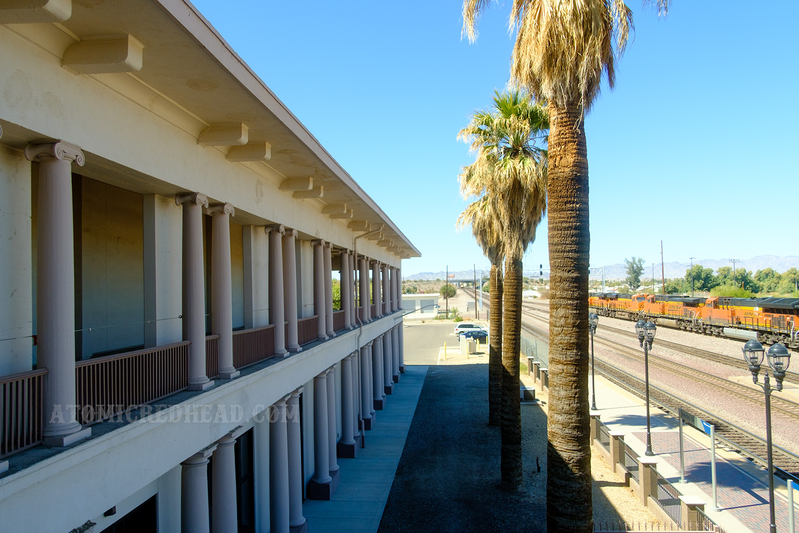 Looking out over the railroad tracks from the second story balcony. Tall palm trees stand between the building and the tracks.