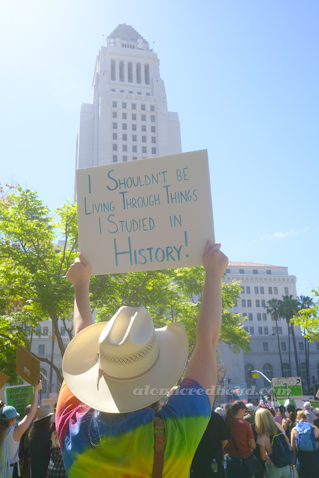 Myself, seen from behind, holding up a sign with "I Shouldn't be Living Through Things I Studied in History!" with LA City Hall visible in the background.