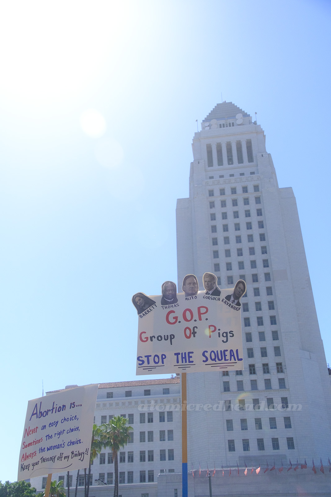 With the iconic LA City Hall in the background a large sign reads "G.O.P. Group of Pigs Stop the Squeal"