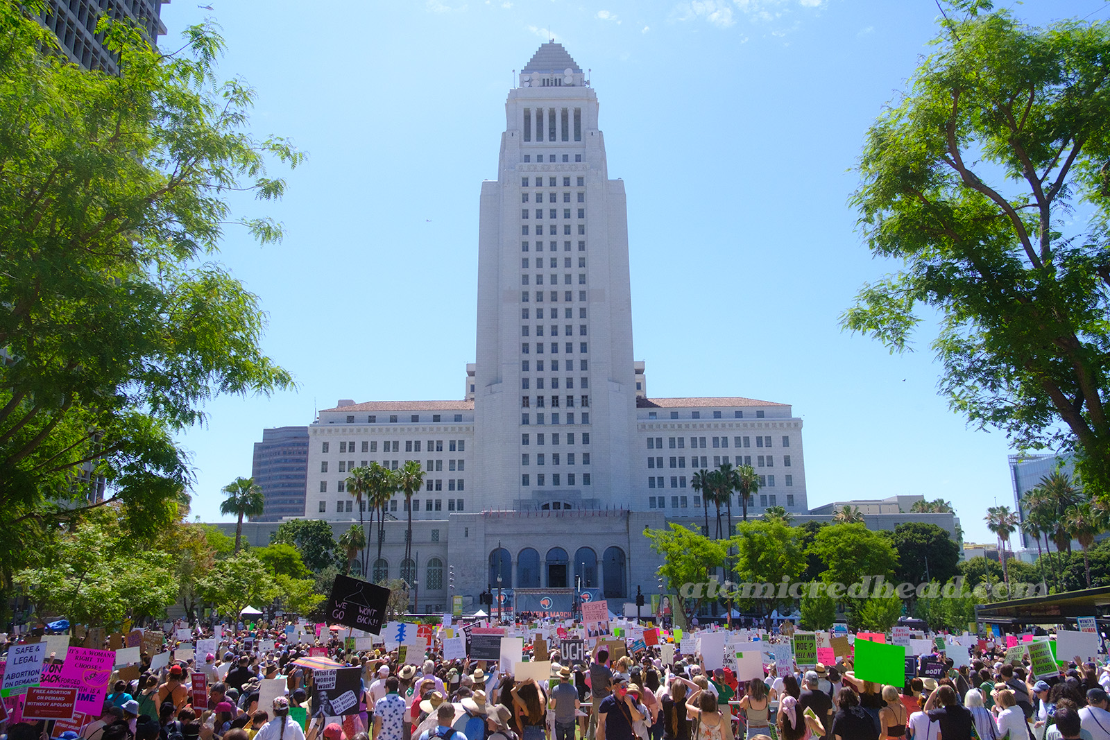 LA City Hall stands tall over a lawn full of people protesting.