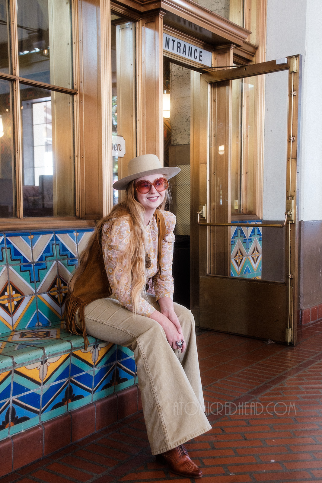 Myself, seated outside Homebound, wearing a cream cowboy hat, fringe leather vest, floral shirt, and tan corduroy pants.