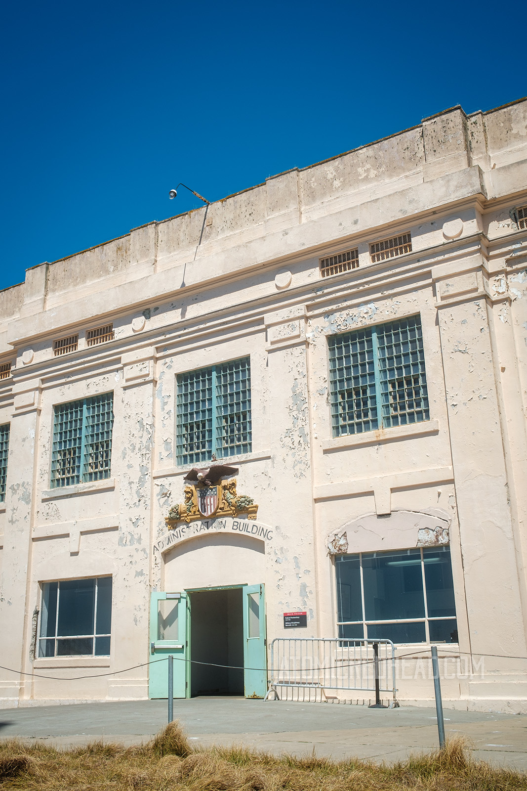 The exterior of the administration building, a smaller, two story building, which still has bars on the windows, and an eagle above the door.