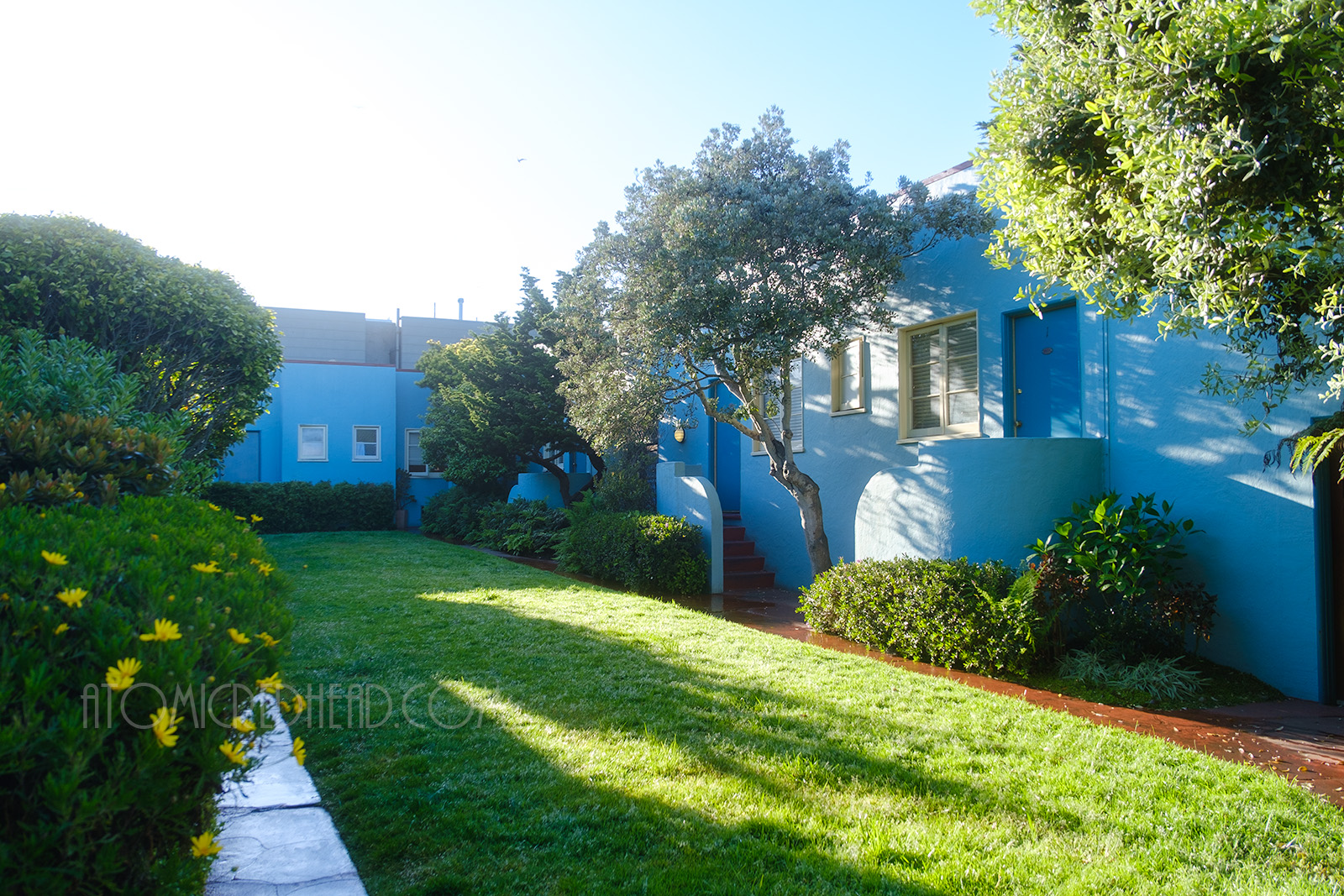 An open courtyard between the rooms features a long green lawn.