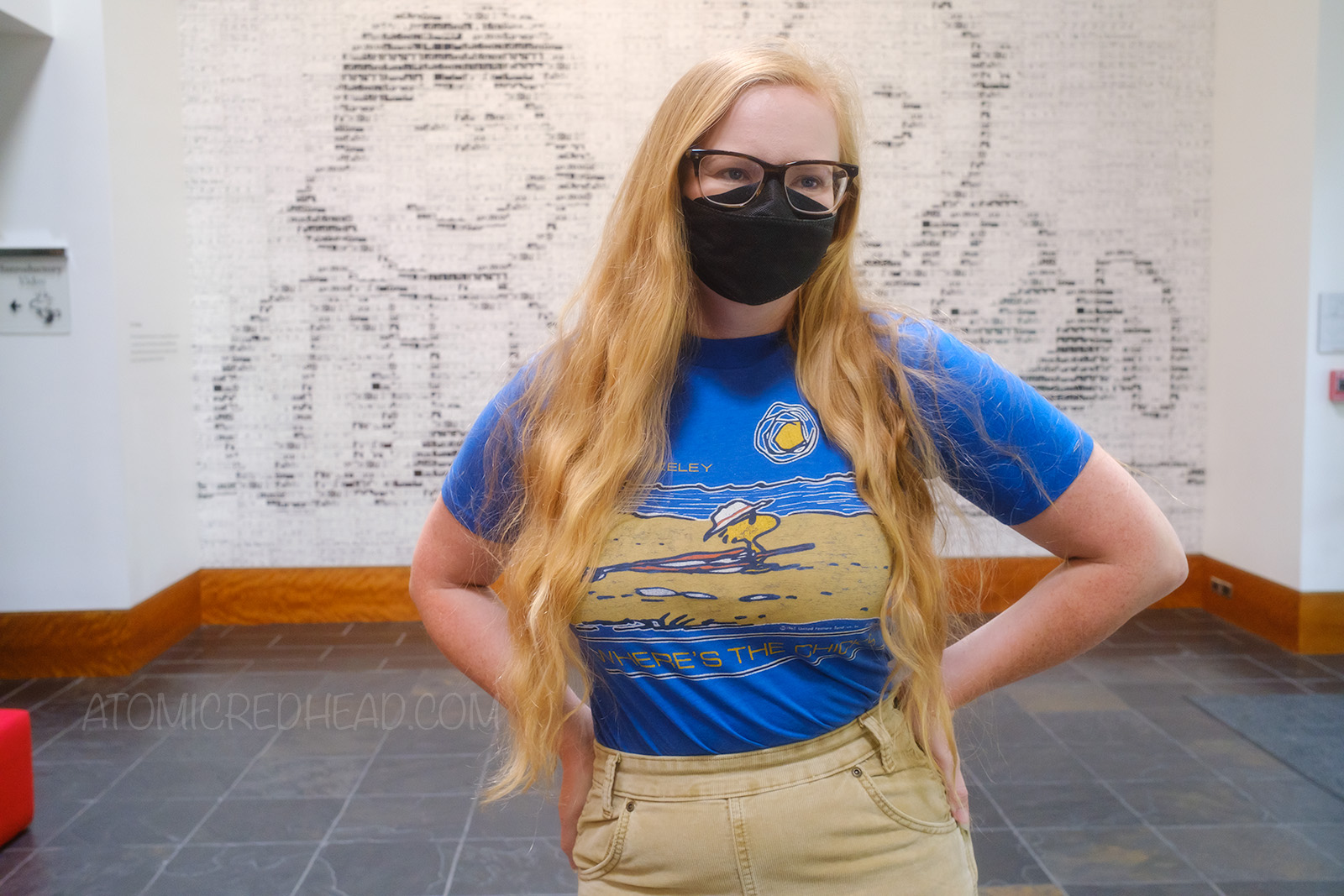 Myself, wearing a blue shirt with Woodstock at the beach, at the bottom it reads "Where's the Chicks?, standing in front of a large mosaic made of tiles of various Peanuts strips designed to show Lucy holding a football, and Charlie Brown running to kick it.