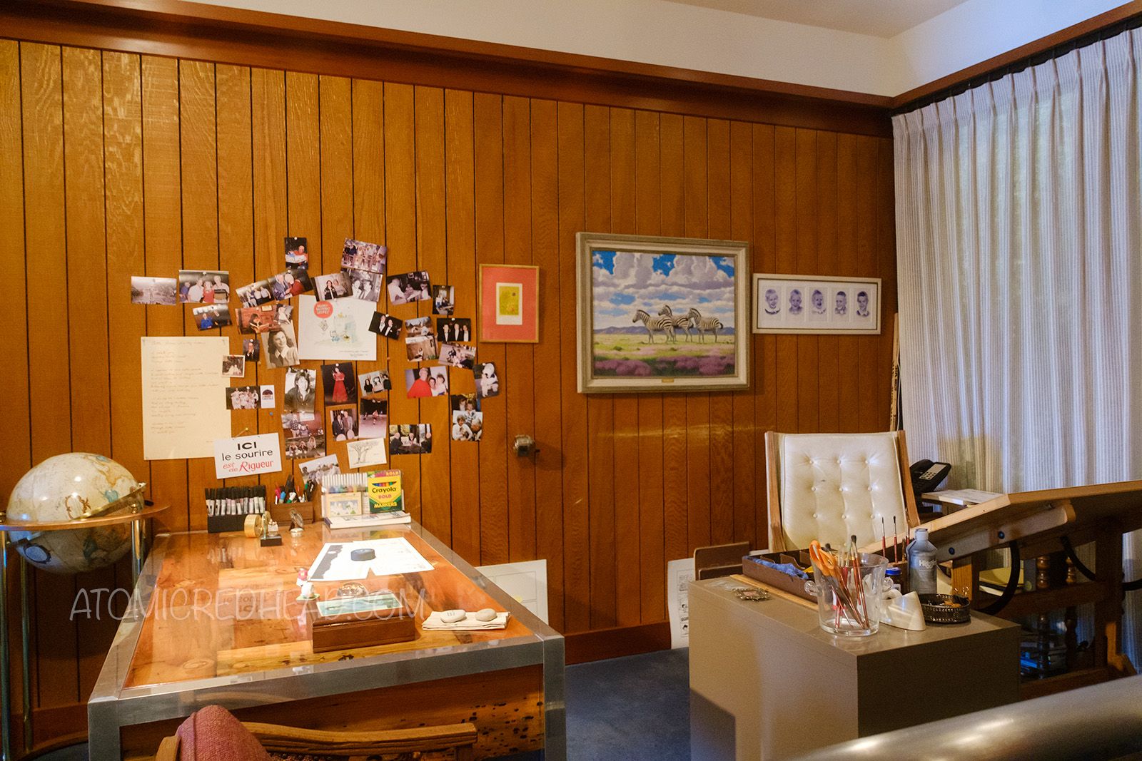 Schulz's office, with a desk and drawing table. Various photographs are tacked up on the wall, and a painting of zebras hangs behind the chair.