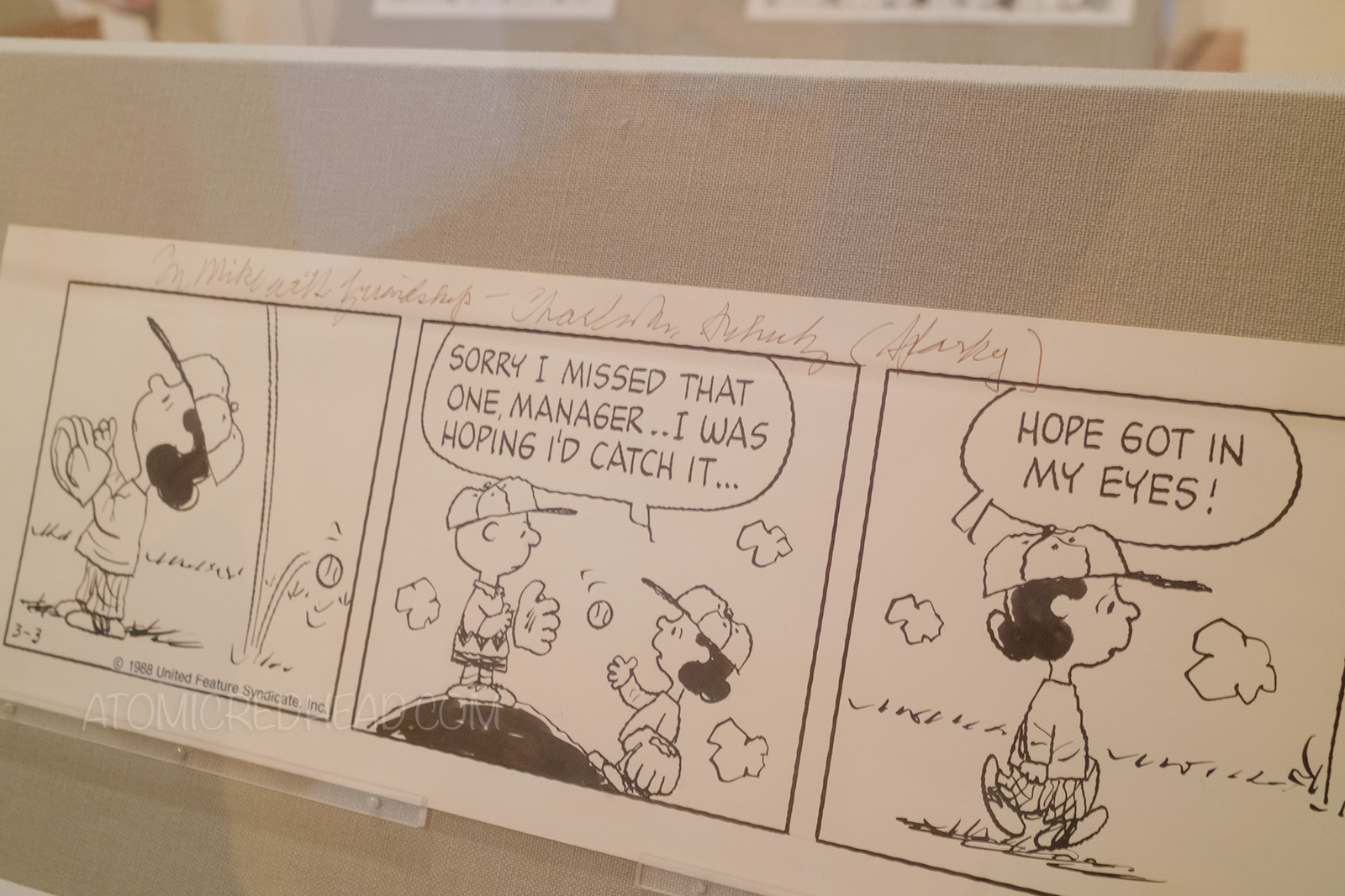 Original strip of Lucy missing catching a base ball, she returns it to Charlie Brown and walks away, her speech bubbles read "Sorry I missed that one manager..I was hoping I'd catch it. Hope got in my eyes." Across the top in pencil reads "To Mike with friendship -Charlies M. Schulz (Sparky)