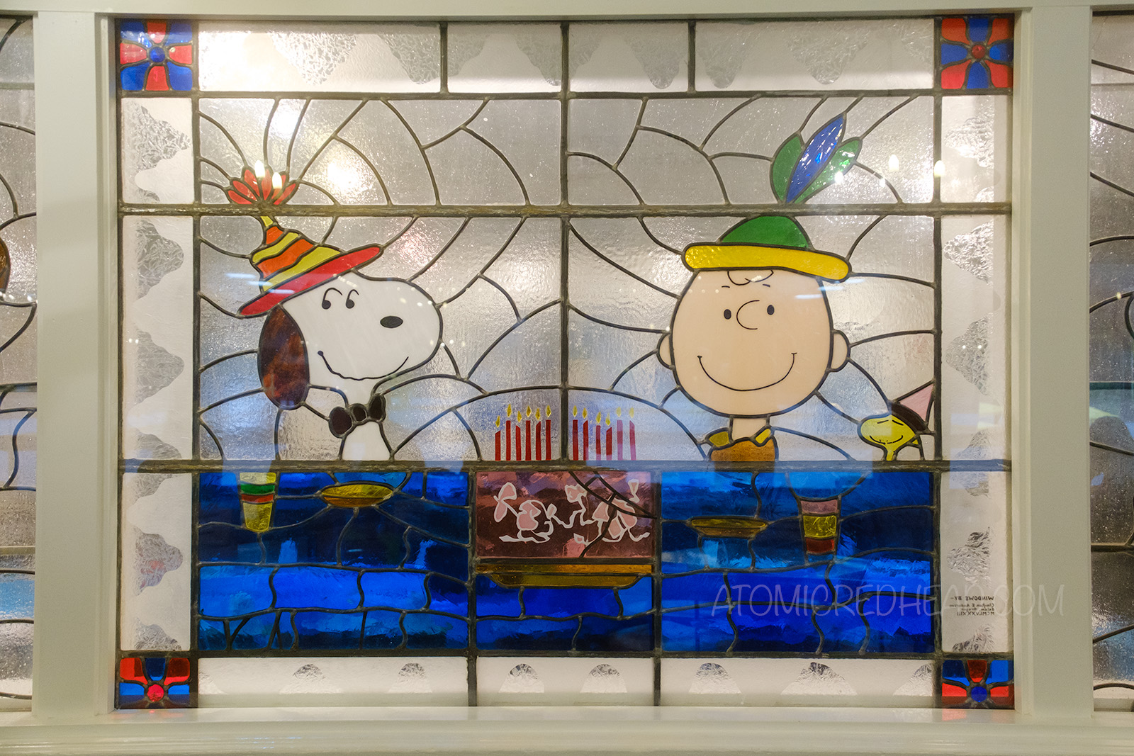 A stained glass featuring Snoopy and Charlie Brown wearing party hats and looking at a birthday cake.