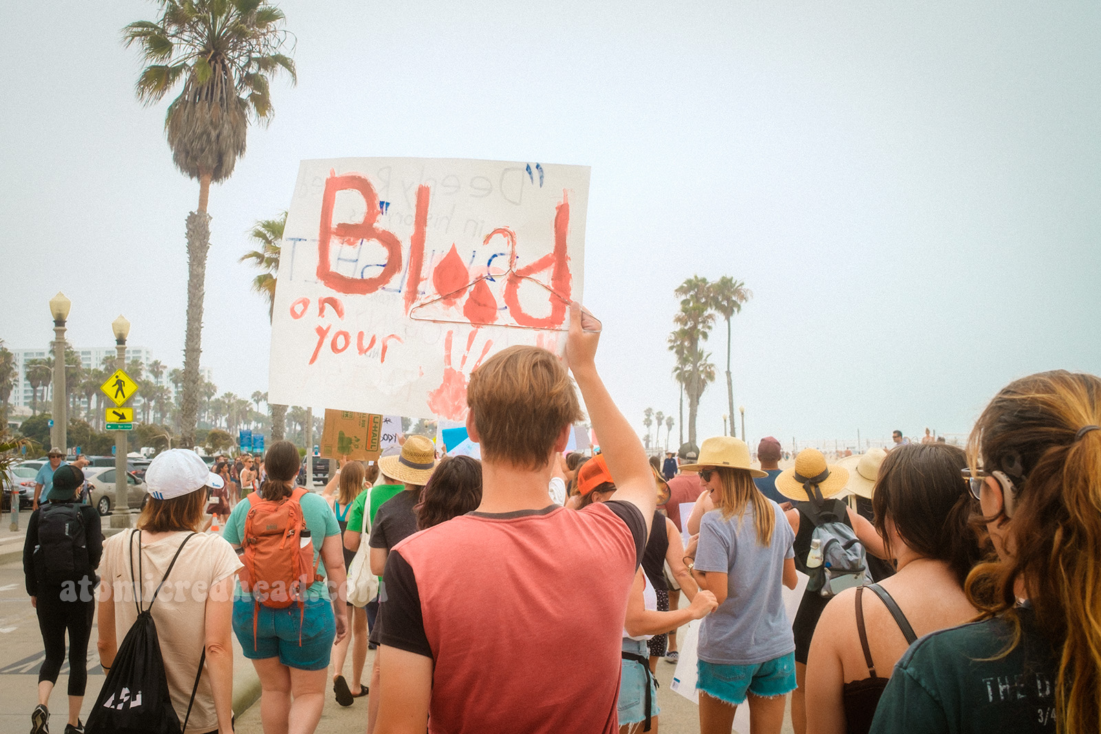 A person holds up a sign reading "Blood is on your" followed by bloody handprints.