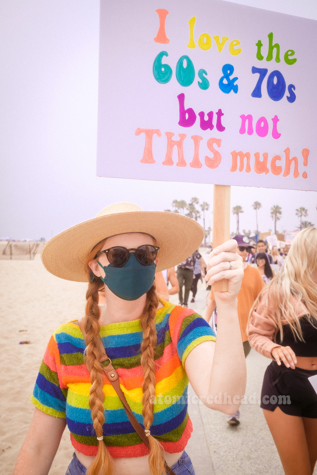 Myself, wearing a rainbow terry cloth crop top and large straw hat, holding a sign reading "I love the 60s & 70s but not THIS much!"