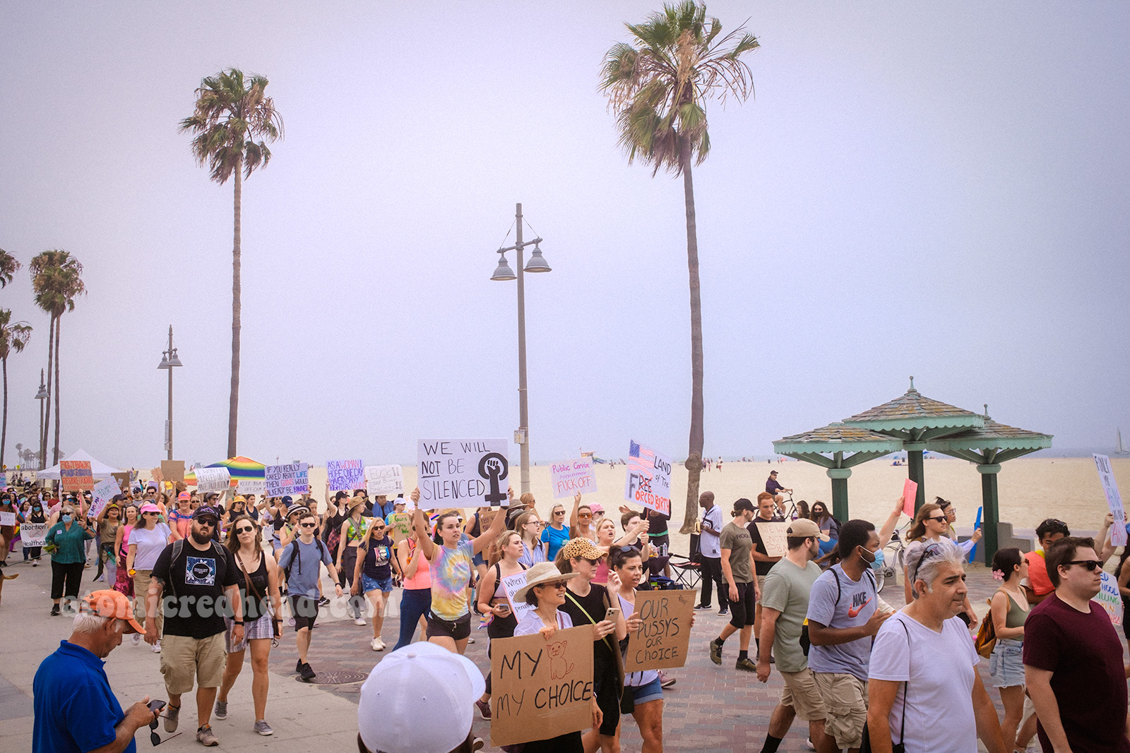 Protestors walk along the sandy beach, some signs read "We will not be silenced" "Our pussys our choice"