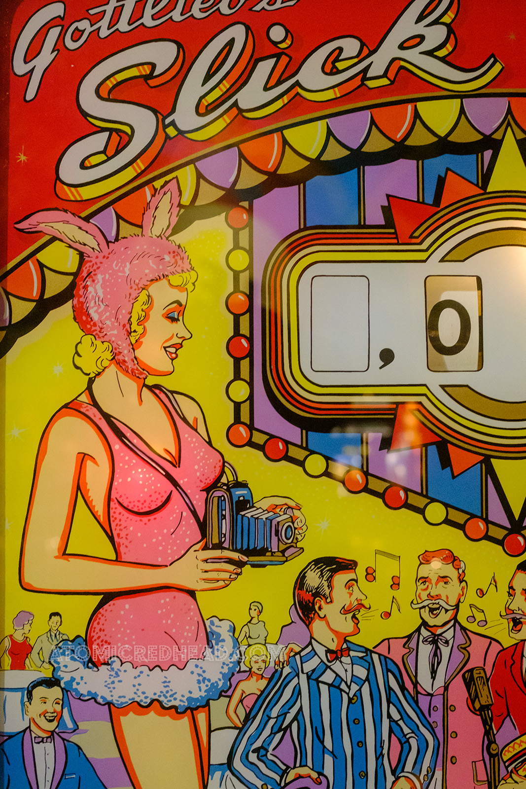 Close-up of a portion of the backglass for Slick Chick, which features a girl in a pink showgirl bunny outfit holding a camera.