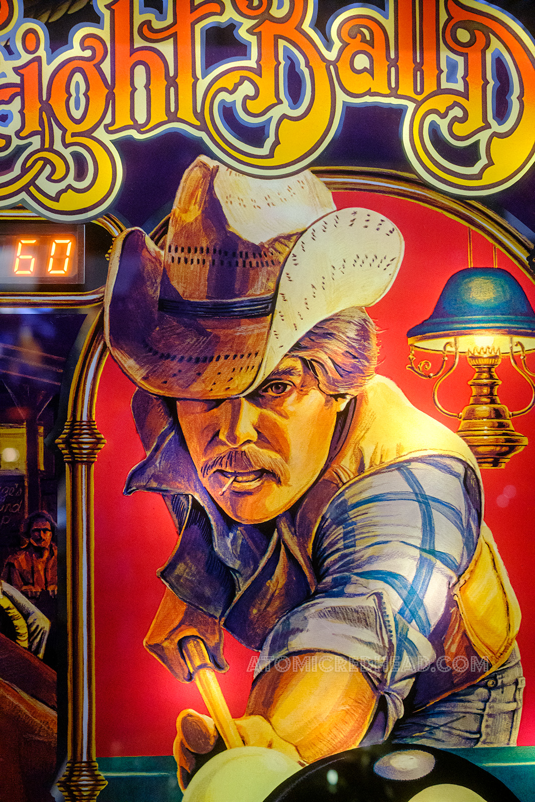 Close-up of Eight Ball Deluxe, which features a mustached cowboy holding a pool cue, wearing a straw cowboy hat, blue plaid shirt and vest.
