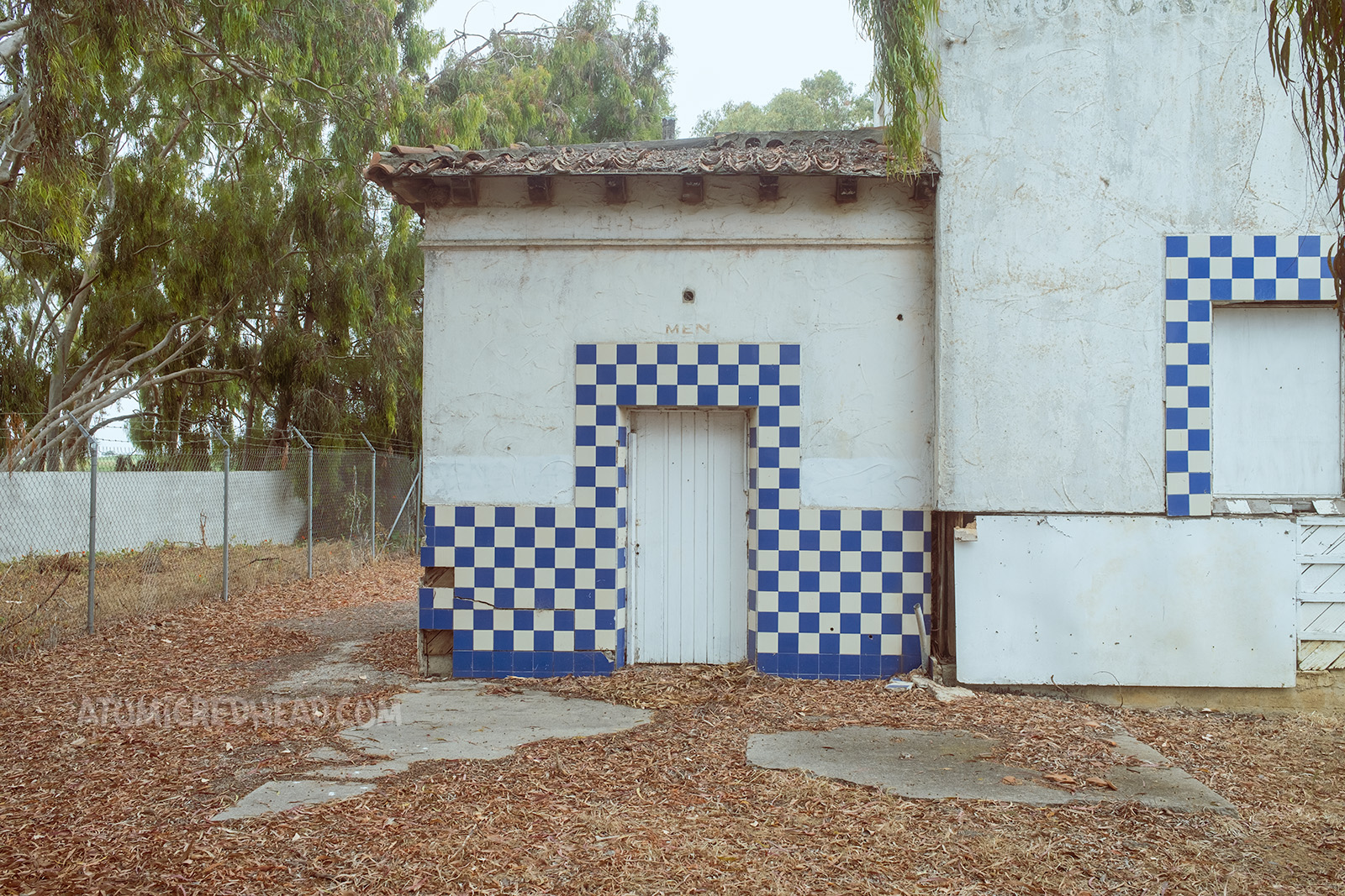 Close-up of the boarded doorway for the mens room, which is framed by blue and white tiles.