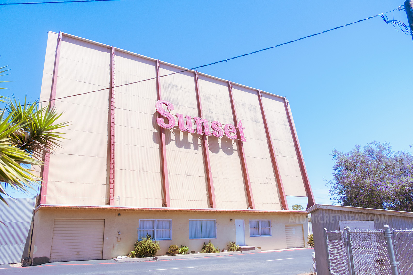Back of the Sunset Drive-In screen, which is painted yellow with red lines going down every ten feet, with large red letters reading "Sunset"