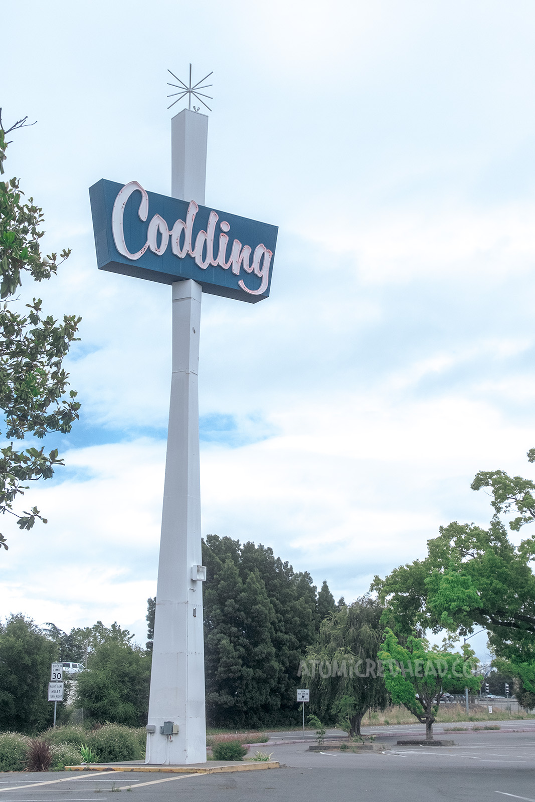 A tall white tower leads up to a blue sign reading "Codding" in neon script, and topped with a sputnik burst.