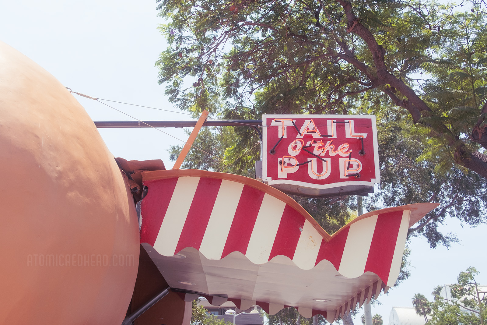 The red and white stripe awning of the Tail O' The Pup, with a small red and white neon sign reading "Tail o'the Pup"
