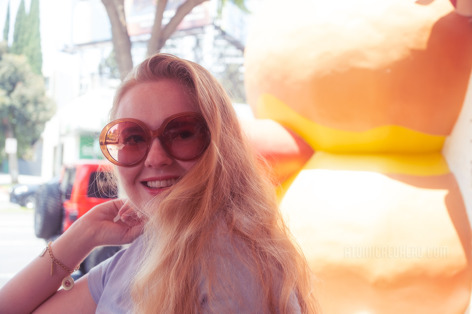 Myself, wearing a light blue shirt with rainbow script reading "93/KHJ Boss 30" and red and yellow corduroy shorts, seated at a table, the massive hot dog shaped building behind me. 