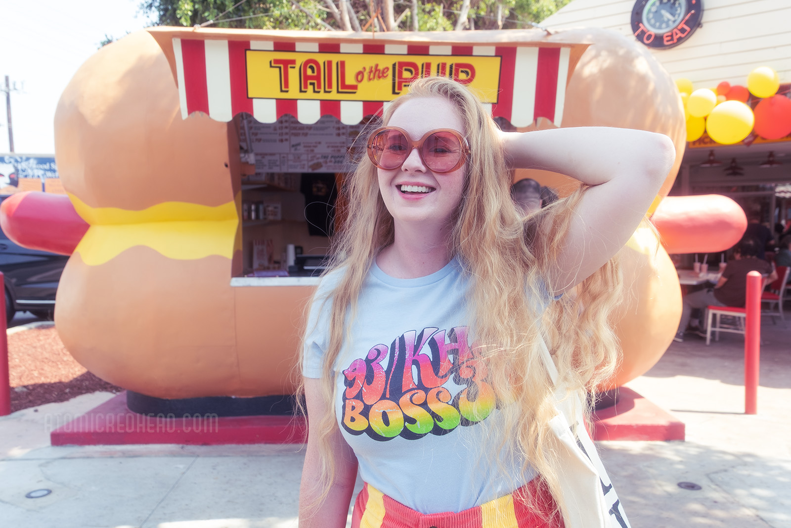 Myself, wearing a light blue shirt with rainbow script reading "93/KHJ Boss 30" and red and yellow corduroy shorts, standing in front of the massive hot dog shaped building.